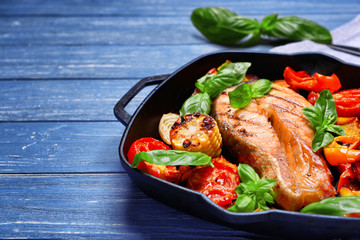 Iron cast pan with slice of red fish and vegetables on gray wooden background