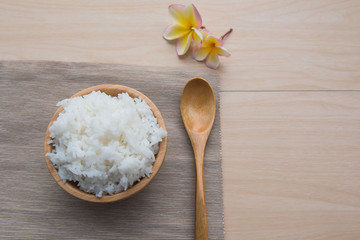 Cooked rice in a wooden bowl and spoon on a wood background.
