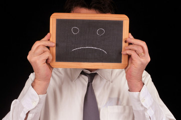Homme tenant une ardoise avec un visage triste dessiné dessus