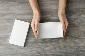 Female hands with white open box on wooden background