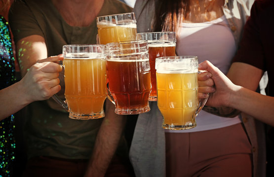 People clinking mugs with beer in pub, closeup