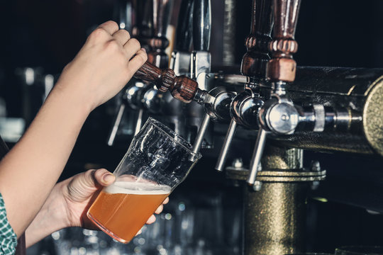 Woman pouring cold beer into glass in bar, closeup