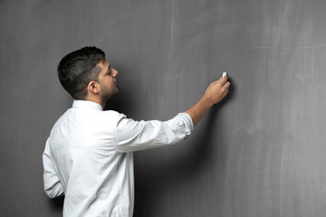 Handsome young teacher writing on blackboard