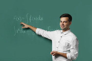Handsome young teacher explaining math formulas written on blackboard