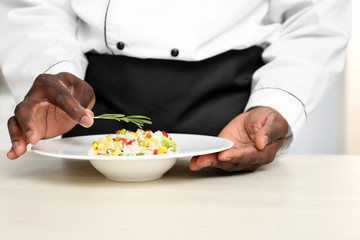 African American chef adding rosemary to tasty salad in kitchen, closeup