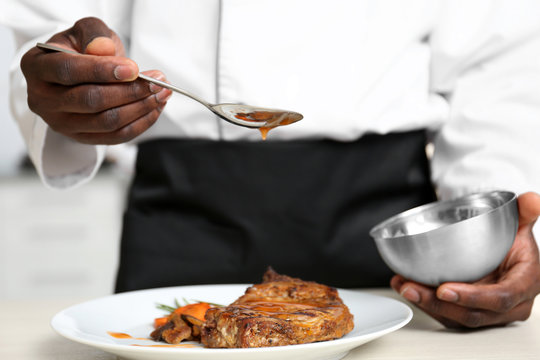 African American chef pouring sauce on tasty meat in kitchen, closeup