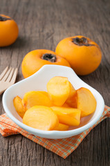 kitchen table with slice fresh orange persimmon on white plate.