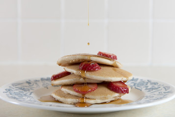 Large stack of golden pancakes covered in strawberries and syrup. 