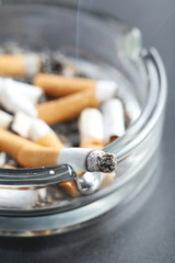Cigarette butts with ash in ashtray on black background