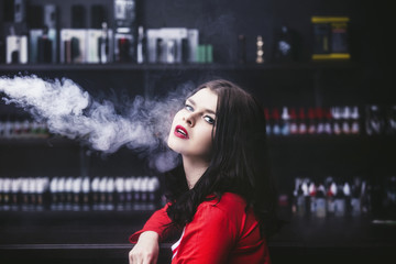 Young beautiful brunette woman with fashion makeup at the bar with a with vapor from electronic...