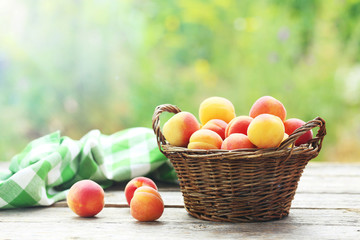 Fototapeta na wymiar Fresh apricots in basket on a grey wooden background, outdoors