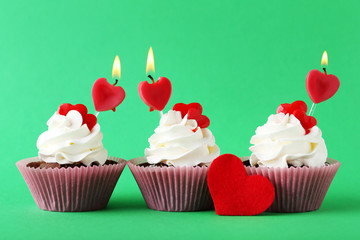Tasty cupcakes with candles on green background