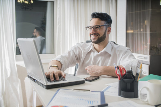 male freelance sitting in an office behind a computer laptop  smiling think and dream