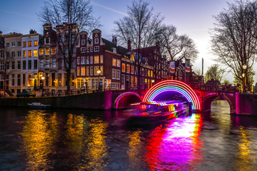 Fototapeta premium Amsterdam, Holandia - 10 stycznia 2017: łodzie wycieczkowe pędzą w kanałach nocnych. Instalacje świetlne na nocnych kanałach Amsterdamu w ramach Festiwalu Światła. 10 stycznia 2017 r. W Amsterdamie - Holandia.