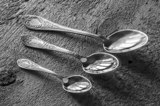 Three silver spoons of various sizes on a background of wooden boards with texture..Black and white photo..
