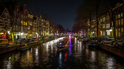 Fototapeta na wymiar AMSTERDAM, NETHERLANDS - JANUARY 11, 2017: Beautiful night city canals of Amsterdam with moving passanger boat. January 11, 2017 in Amsterdam - Netherland.