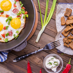 Fried eggs in pan with tomatoes and green fresh onion.