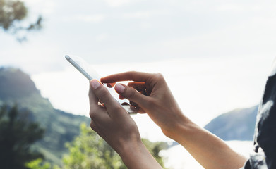 Hipster girl texting message on smartphone mobile close up, view tourist hands using gadget phone on device on background perspective mountains and sky landscape; finger touch screen cellphone mockup