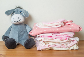 Pile of clothes for newborn girl on wooden background with toy
