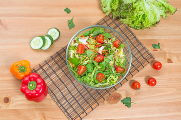 Salad of fresh vegetables and green on wooden background, top view.