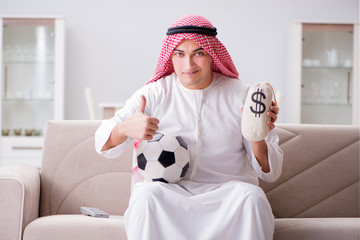 Young arab man watching football sitting on sofa