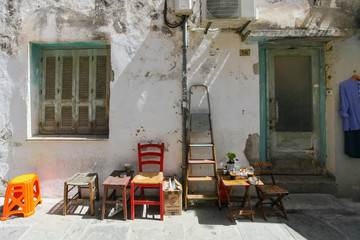 Wooden chairs, ladder, small tables with cups of frappe near the outside wall of old house located...