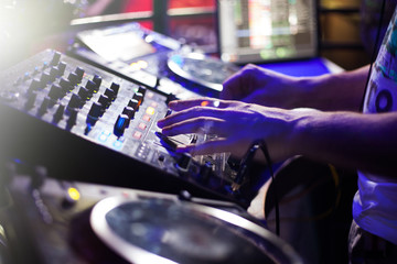 DJ playing music at mixer closeup and mixes the track in the nightclub at party
