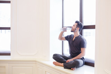 Naklejka na ściany i meble Beautiful woman drinking water while holding yoga mat in fitness studio
