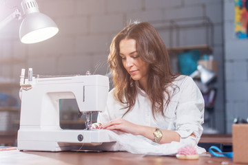 Attractive Caucasian seamstress working stitching with sewing machine at her workplace in studio ...