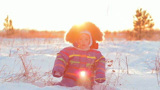 Happy child boy walks in the snow and falls at sunset