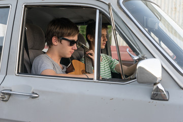 Naklejka premium Two young boys in the car. boy plays the guitar in the car. cheerful company of young people. journey together. fun pastime.