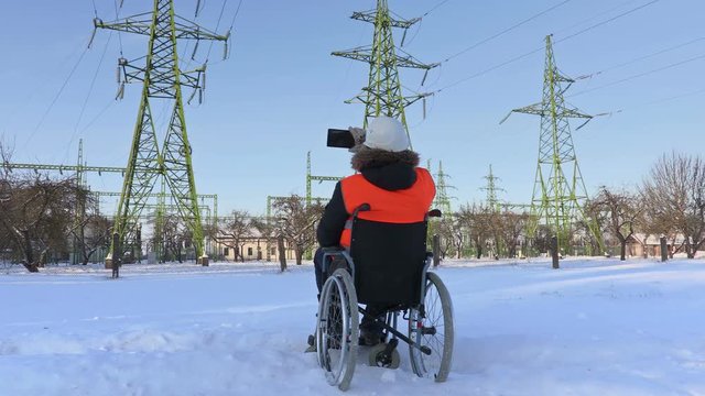 Disabled worker on wheelchair take pictures near to high-voltage lines
