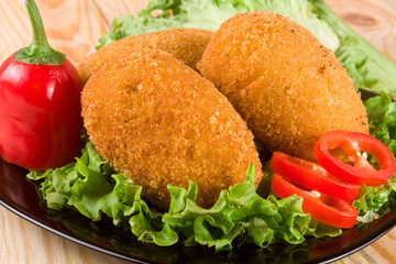 three fried breaded cutlet with lettuce on a black plate and wooden background