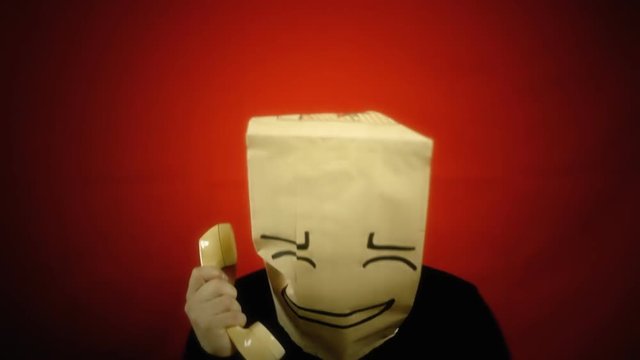 A shy bashful breadbag face, in a conversation on a retro rotary telephone. Close-up shot.
