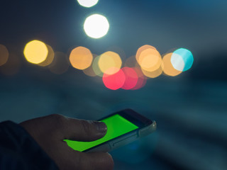 Closeup of male hands using modern smartphone at night, bokeh light in blurred background