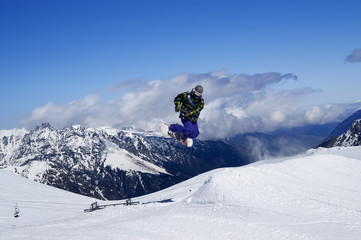 Snowboarder jumping in terrain park at snow mountain on sunny wi