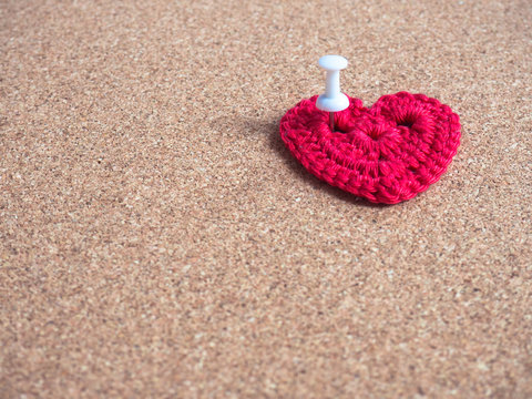 Red crocheted heart pinned on cork board.