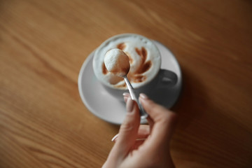 Woman holding spoon with cappuccino foam in cafe