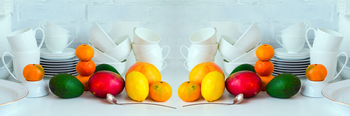 White porcelain dish and bright fresh fruits on white kitchen table. Concept of healthy eating and cooking. Copy space. Wide panoramic.