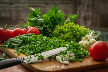 Sliced green onions, tomatoes, parsley and a knife on a cutting Board. Wooden background. Culinary websites and publications