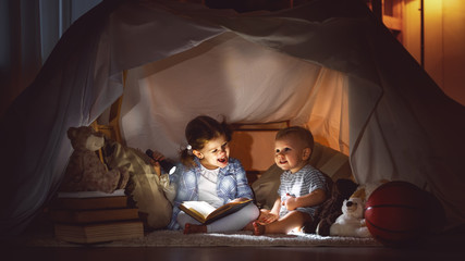 Obraz na płótnie Canvas children boy and girl reading book with flashlight in tent