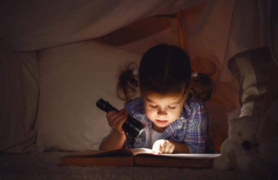 child girl with a book and a flashlight and teddy bear before go