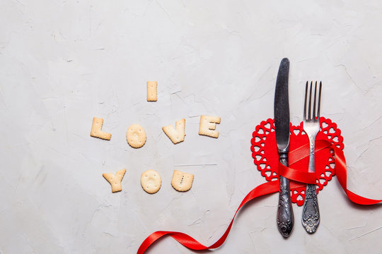 Valentines day table setting with fork, knife and cookies I LOVE YOU on gray background, Top view