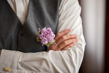 Wedding details, crossed arms of groom with flower boutonniere on grey vest and wedding ring on his finger
