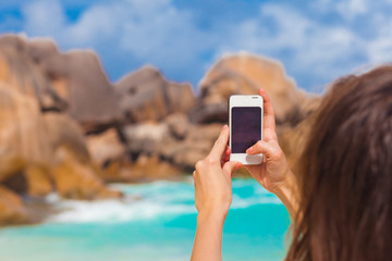 woman taking photo on sea beach with mobile smart phone camera at Grand Anse. La Digue, Seychelles