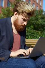 Handsome bearded hipster with serious emotion on red brick wall background. High detailed close up portrait of european 25 years man in summer time.