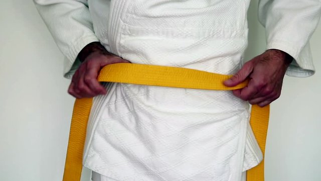 martial arts clothes, judo gi - a man tighten his yellow belt on a white kimono