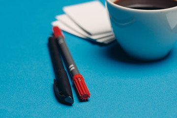 mug of coffee on a blue background, business card on the table, pen