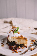 Cheesecake, served with a scoop of ice cream, mint and cranberry jam on a round white plate with crumpled old gray dishcloth in the background