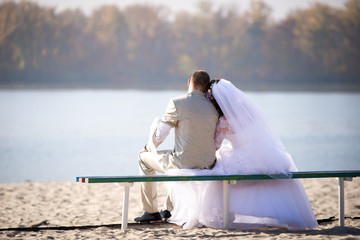 The bride with the groom in white sitting on the beach.
